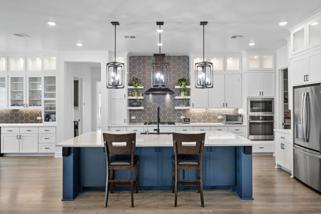 Professional real estate photography of a modern luxury kitchen with white cabinets, large island, pendant lighting, and custom finishes
